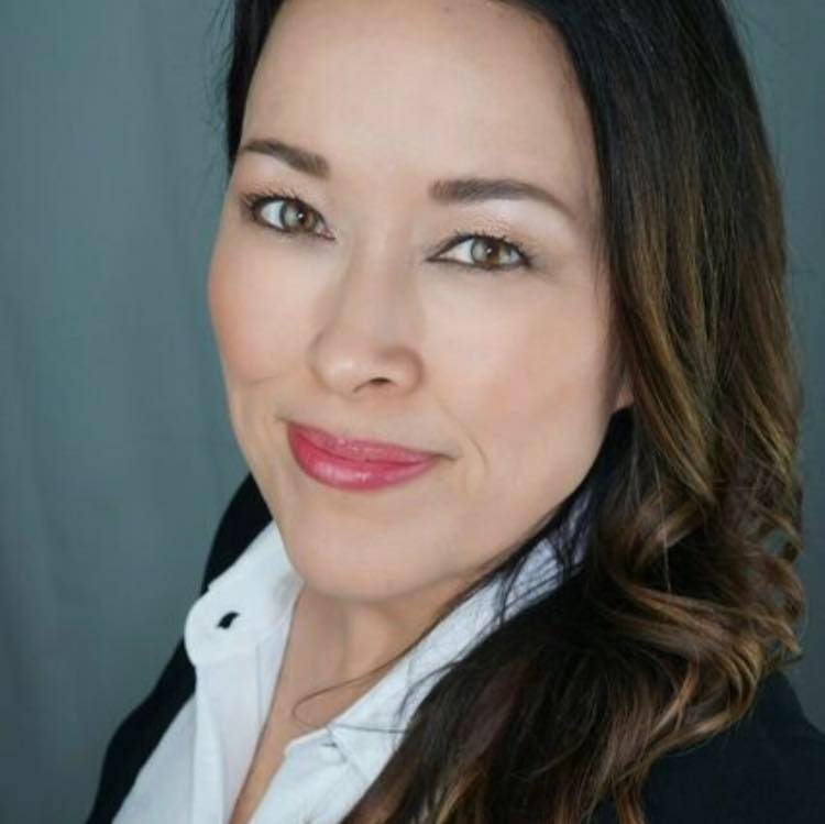 A woman with long brown hair and light makeup smiles slightly at the camera. Family Nurse Practitioner Mary McMillin wears a white collared shirt and dark blazer, standing against a neutral-colored background.