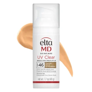 A bottle of EltaMD UV Clear Broad Spectrum SPF 46 Tinted Face Sunscreen stands in front of a tan-colored smear of the product. The label highlights protection for acne and rosacea-prone skin.